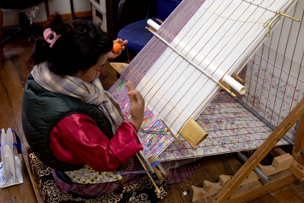 Travel to Bhutan from Europe. A woman weaving Bhutanese National dress call Kira for the women